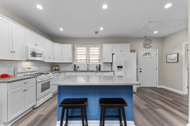 kitchen featuring a kitchen island, white appliances, a breakfast bar area, dark wood-style floors, and a sink
