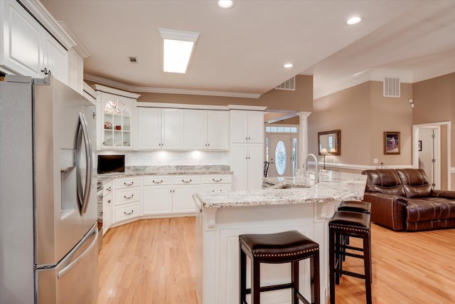 kitchen with stainless steel refrigerator with ice dispenser, a kitchen bar, sink, white cabinetry, and decorative columns