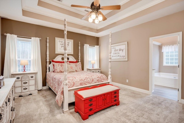 carpeted bedroom with a raised ceiling, crown molding, connected bathroom, and ceiling fan