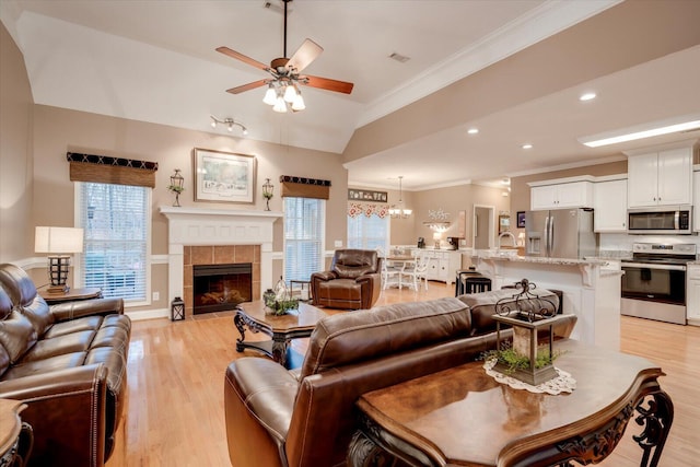 living room with sink, crown molding, ceiling fan, a tiled fireplace, and light wood-type flooring