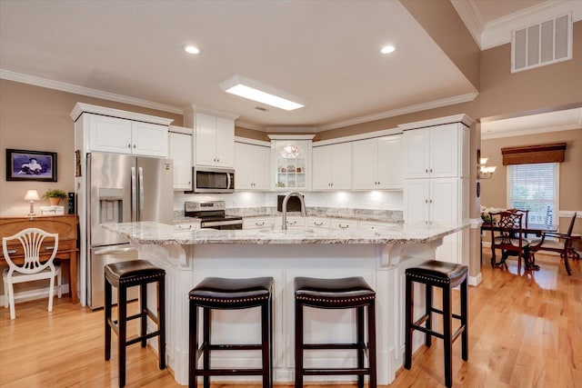 kitchen with a breakfast bar area, appliances with stainless steel finishes, white cabinetry, light stone counters, and decorative backsplash