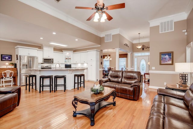 living room with sink, light hardwood / wood-style flooring, decorative columns, ornamental molding, and ceiling fan with notable chandelier