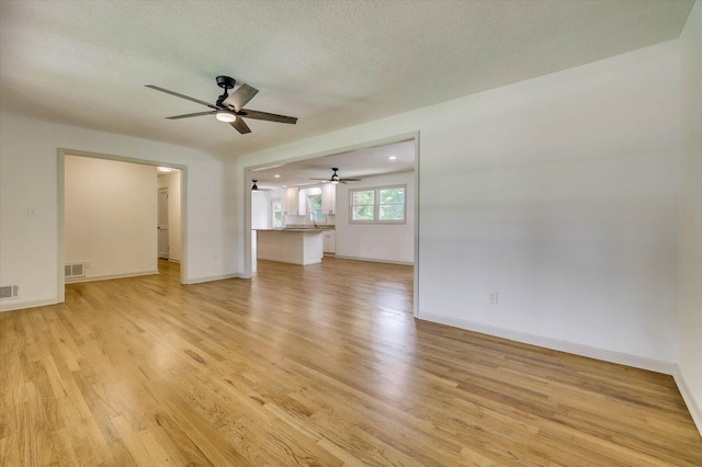 unfurnished living room with a textured ceiling, light hardwood / wood-style flooring, and ceiling fan