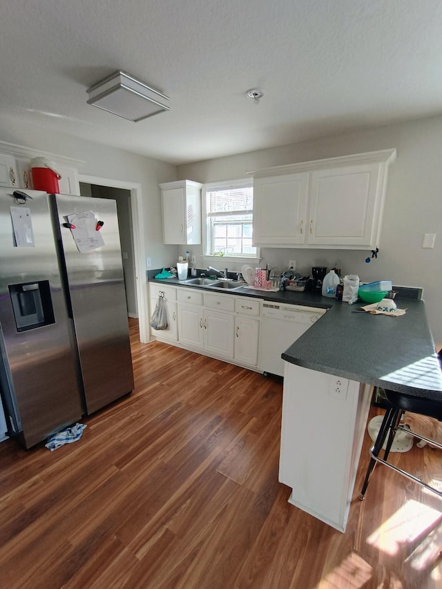 kitchen with dark countertops, stainless steel fridge with ice dispenser, dishwasher, a peninsula, and a sink