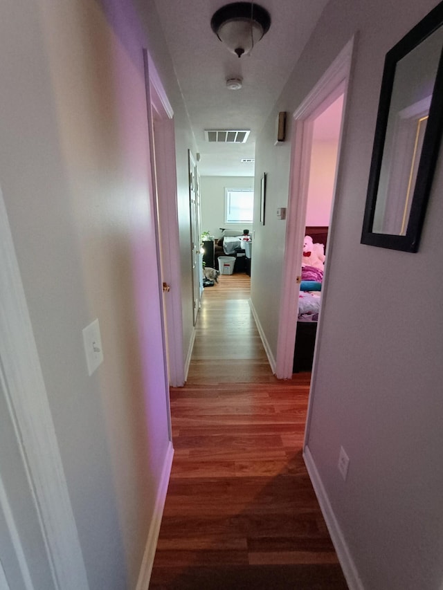 corridor featuring visible vents, baseboards, and wood finished floors