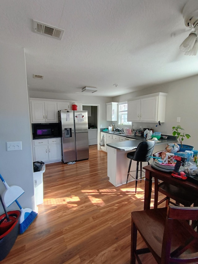 kitchen featuring visible vents, stainless steel refrigerator with ice dispenser, a peninsula, black microwave, and light wood finished floors