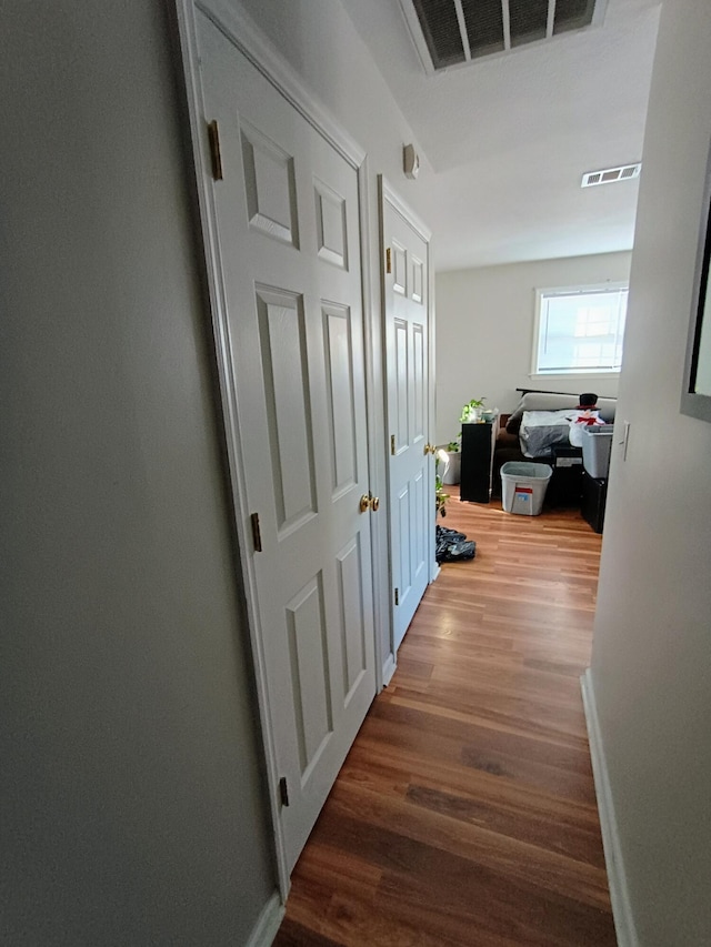 hallway featuring wood finished floors, visible vents, and baseboards