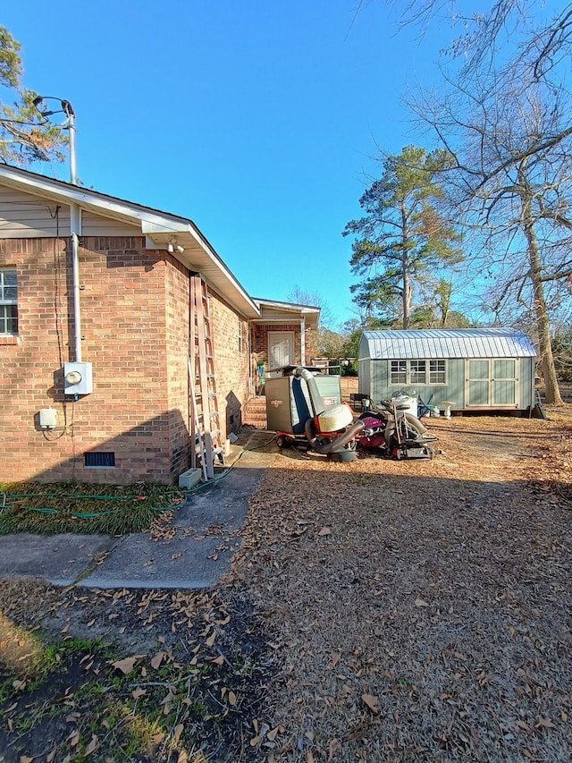 view of property exterior featuring crawl space, a greenhouse, brick siding, and an outdoor structure