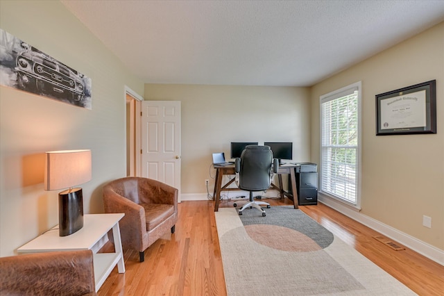 office area with baseboards, light wood-style flooring, and visible vents