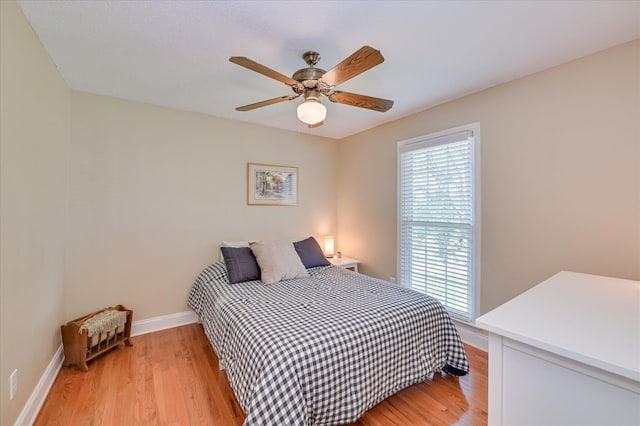 bedroom with a ceiling fan, baseboards, multiple windows, and light wood-style floors