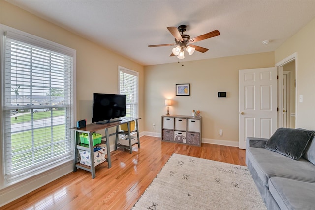 living area with ceiling fan, baseboards, and light wood-style floors