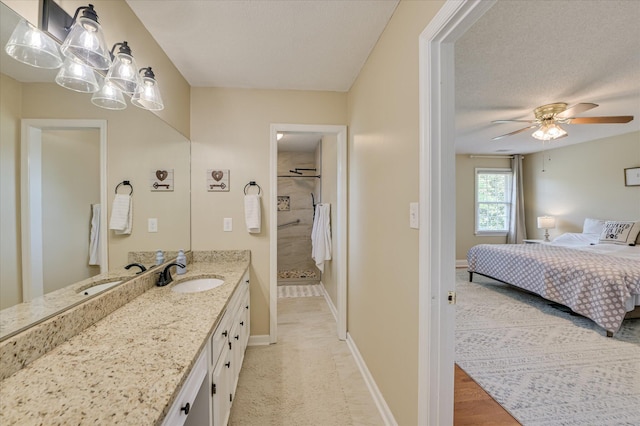 ensuite bathroom with ceiling fan, vanity, a textured ceiling, baseboards, and tiled shower