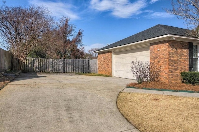 view of side of property with fence, a shingled roof, concrete driveway, and brick siding