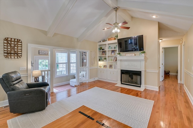 living area with a fireplace with flush hearth, ceiling fan, lofted ceiling with beams, and light wood finished floors