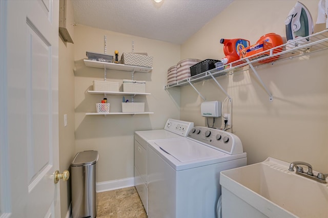 washroom featuring laundry area, a sink, a textured ceiling, baseboards, and washing machine and dryer