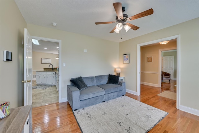 living area with light wood-style floors, baseboards, and a ceiling fan