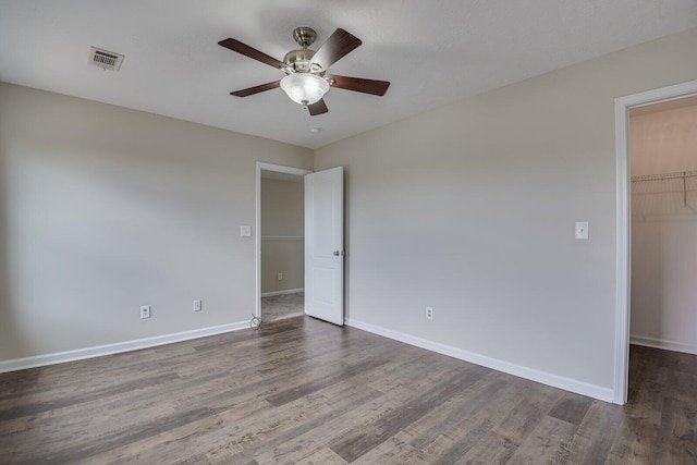 unfurnished bedroom featuring a walk in closet, a closet, ceiling fan, and dark hardwood / wood-style floors