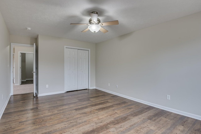 unfurnished bedroom with a textured ceiling, ceiling fan, dark wood-type flooring, and a closet