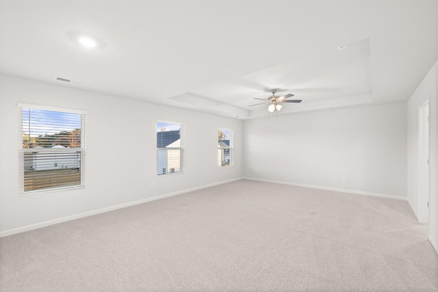 empty room featuring a tray ceiling, light carpet, and ceiling fan