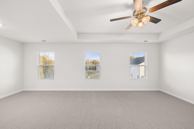 empty room with a raised ceiling, a wealth of natural light, ceiling fan, and carpet