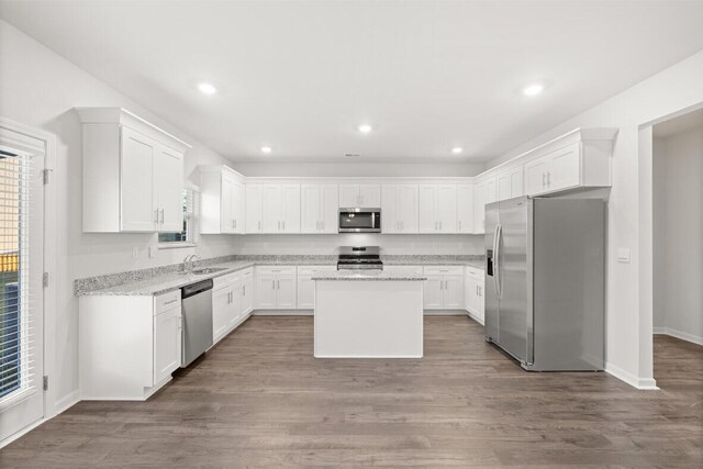 kitchen with white cabinets, stainless steel appliances, a kitchen island, and light stone counters