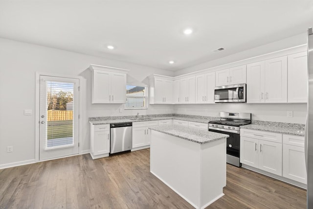 kitchen featuring a kitchen island, light stone countertops, appliances with stainless steel finishes, light hardwood / wood-style floors, and white cabinetry