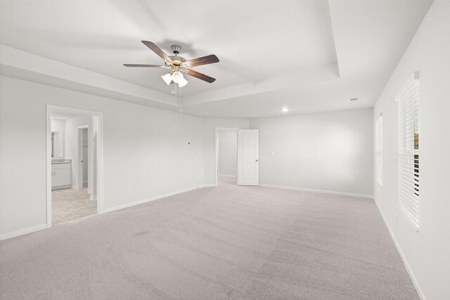 spare room featuring a tray ceiling, light carpet, and ceiling fan