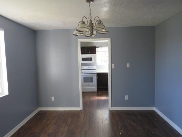 unfurnished dining area with dark wood-style flooring, a notable chandelier, a textured ceiling, and baseboards