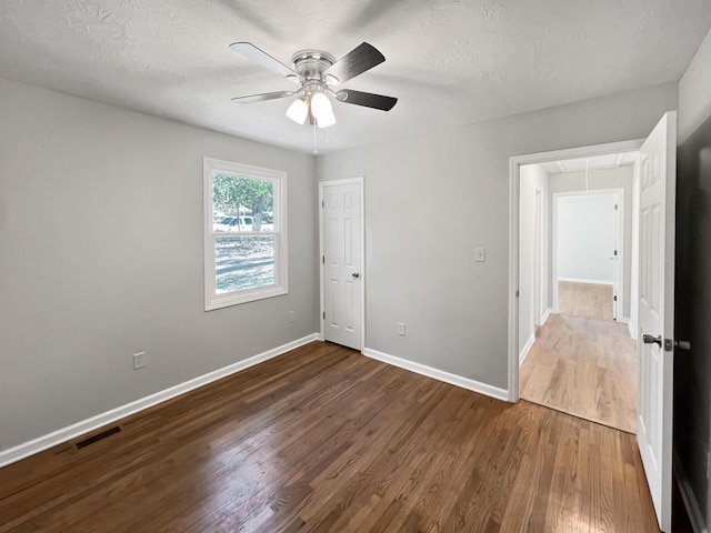 unfurnished bedroom with a textured ceiling, dark hardwood / wood-style floors, and ceiling fan