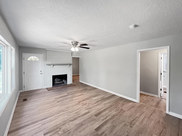 unfurnished living room featuring ceiling fan, light hardwood / wood-style floors, a healthy amount of sunlight, and a brick fireplace