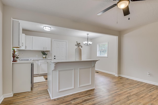 kitchen with white cabinetry, a center island, sink, hanging light fixtures, and light wood-type flooring