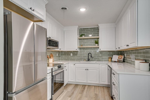 kitchen with a textured ceiling, stainless steel appliances, sink, light hardwood / wood-style floors, and white cabinetry