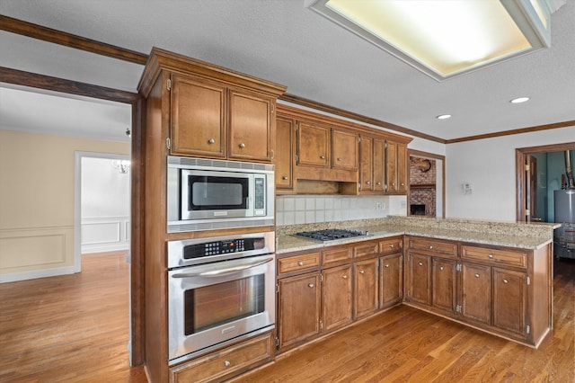 922 Windmill Ln, Evans, GA 30809 - kitchen featuring appliances with stainless steel finishes, light wood-style floors, a peninsula, crown molding, and brown cabinetry