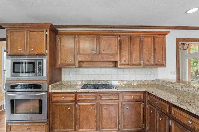 922 Windmill Ln, Evans, GA 30809 - kitchen with appliances with stainless steel finishes, decorative backsplash, light stone countertops, brown cabinets, and a textured ceiling