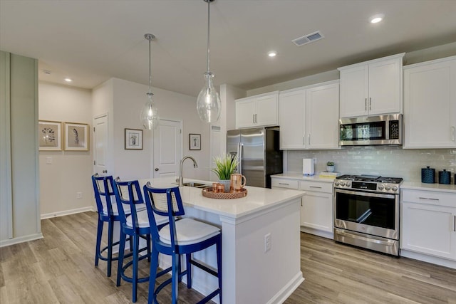 kitchen featuring decorative light fixtures, white cabinets, a kitchen island with sink, and stainless steel appliances