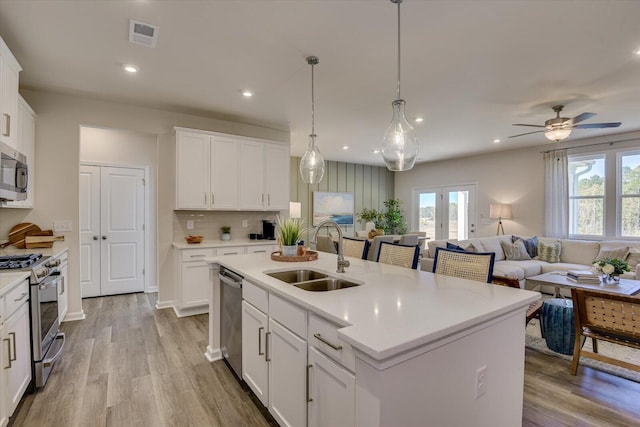 kitchen featuring white cabinets, stainless steel appliances, an island with sink, sink, and hanging light fixtures