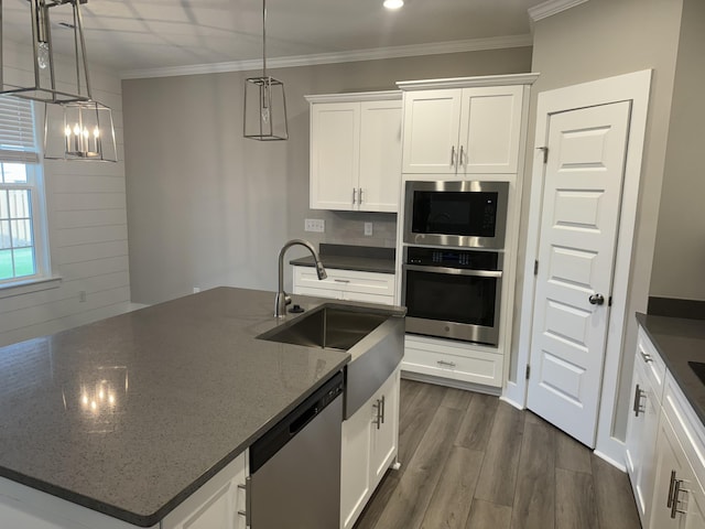 kitchen with stainless steel appliances, dark wood-type flooring, a sink, a center island with sink, and crown molding