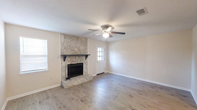 unfurnished living room with visible vents, a ceiling fan, wood finished floors, a stone fireplace, and baseboards