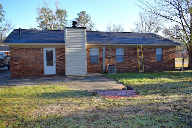 rear view of property featuring a yard, brick siding, central AC unit, a chimney, and a patio area