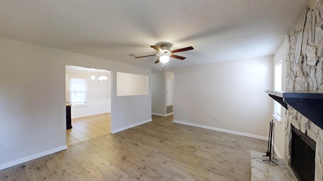 unfurnished living room with visible vents, light wood-style flooring, a fireplace, and ceiling fan with notable chandelier