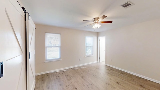 empty room with visible vents, a barn door, light wood finished floors, baseboards, and ceiling fan