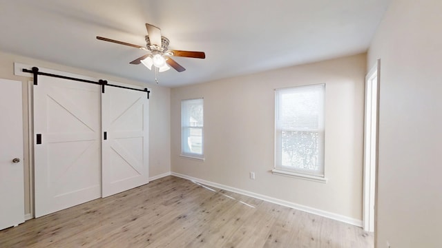 unfurnished bedroom featuring a barn door, light wood-style floors, baseboards, and ceiling fan