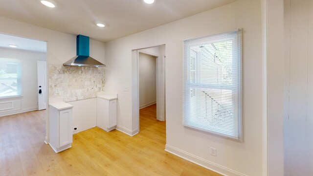 kitchen with wall chimney range hood, tasteful backsplash, light wood-style flooring, light countertops, and recessed lighting