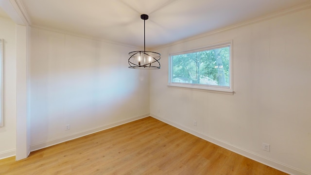 spare room featuring light wood finished floors, crown molding, baseboards, and a chandelier