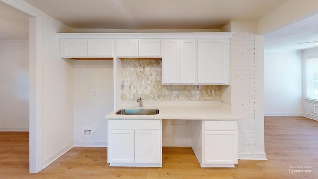 kitchen featuring a sink, decorative backsplash, white cabinets, and light wood-style floors