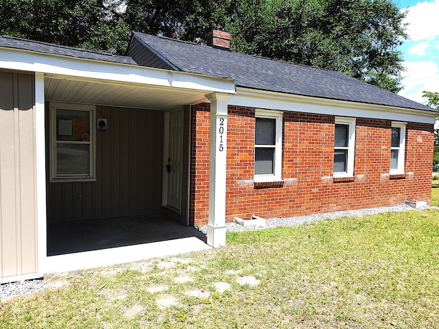 view of front facade featuring a chimney, a front yard, brick siding, and roof with shingles