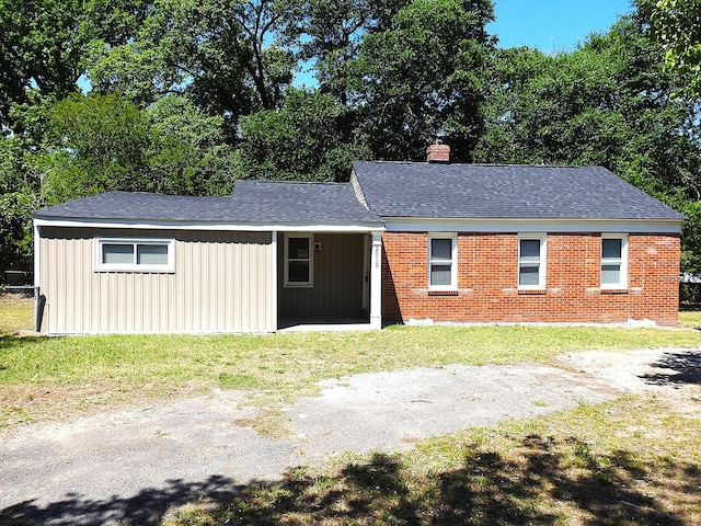 single story home featuring a chimney, board and batten siding, a shingled roof, a front yard, and brick siding