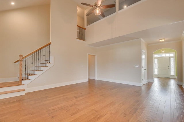 unfurnished living room with wood-type flooring, ornamental molding, ceiling fan, and a high ceiling