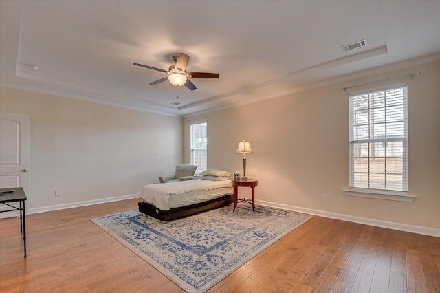 bedroom with ceiling fan, wood-type flooring, a tray ceiling, and ornamental molding