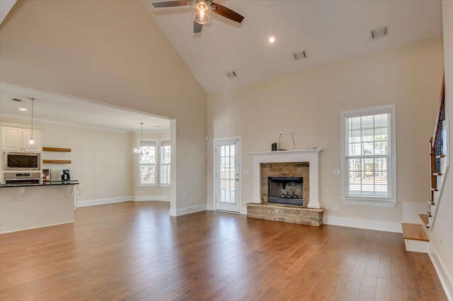 unfurnished living room with a stone fireplace, high vaulted ceiling, light hardwood / wood-style floors, and ceiling fan